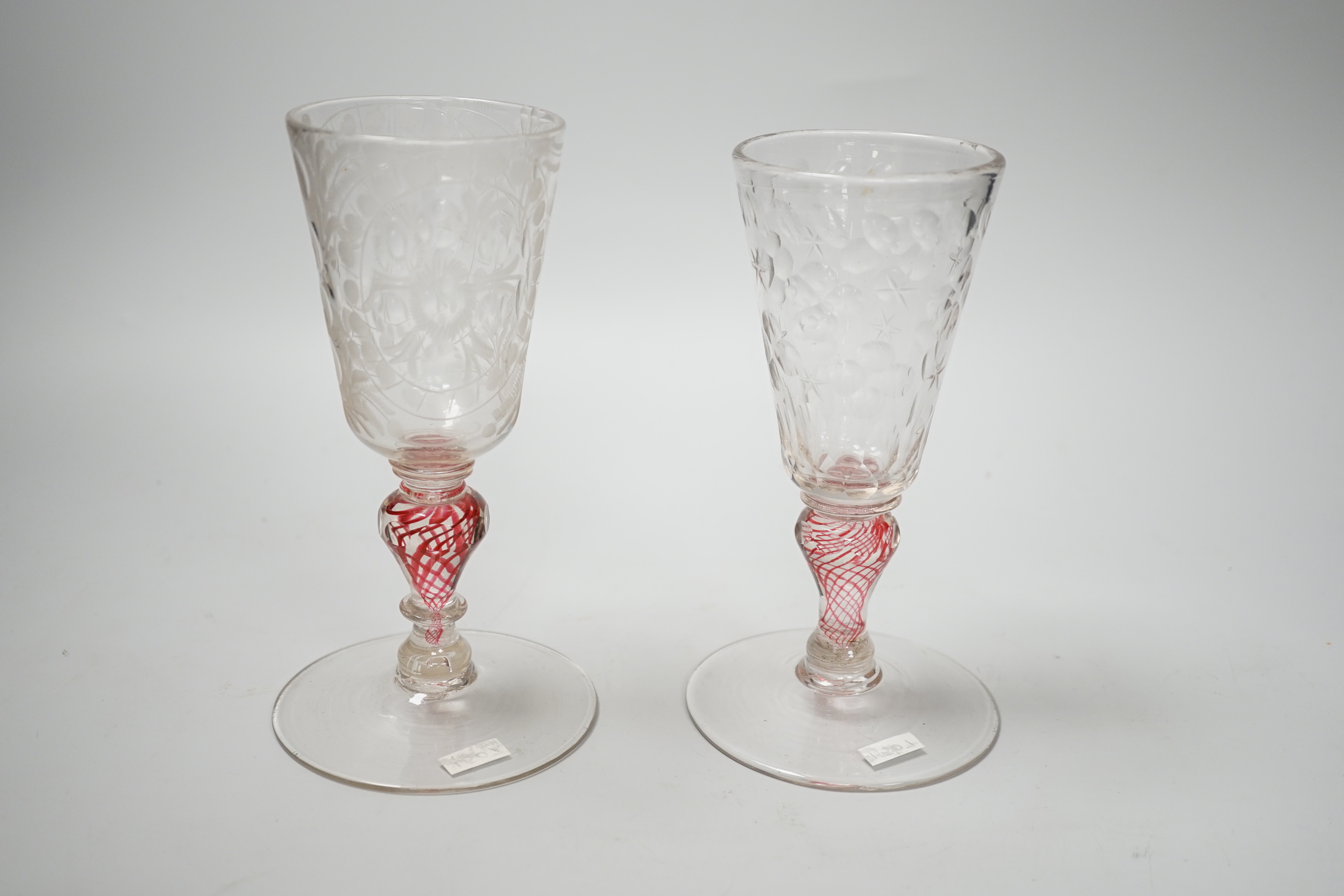 Two similar 18th century Continental goblets, both with elongated bowls heavily engraved with polished roundels, on inverted baluster stems including red colour twists and various collars, conical feet with rough pontils